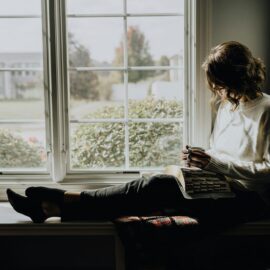 Midlife woman sitting by a window, managing sleep disturbances and perimenopause symptoms.